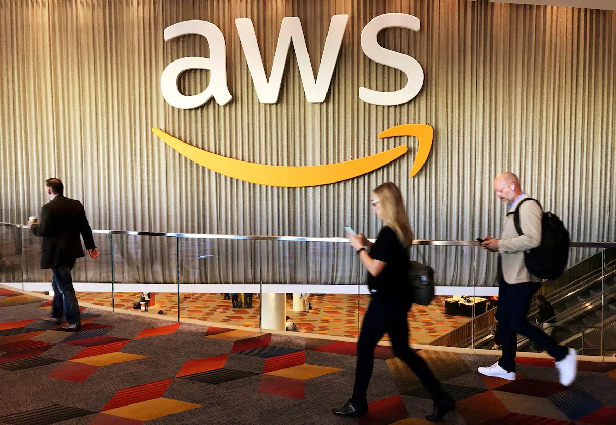 Attendees walking past a large illuminated AWS logo mounted on a wall at an Amazon Web Services event