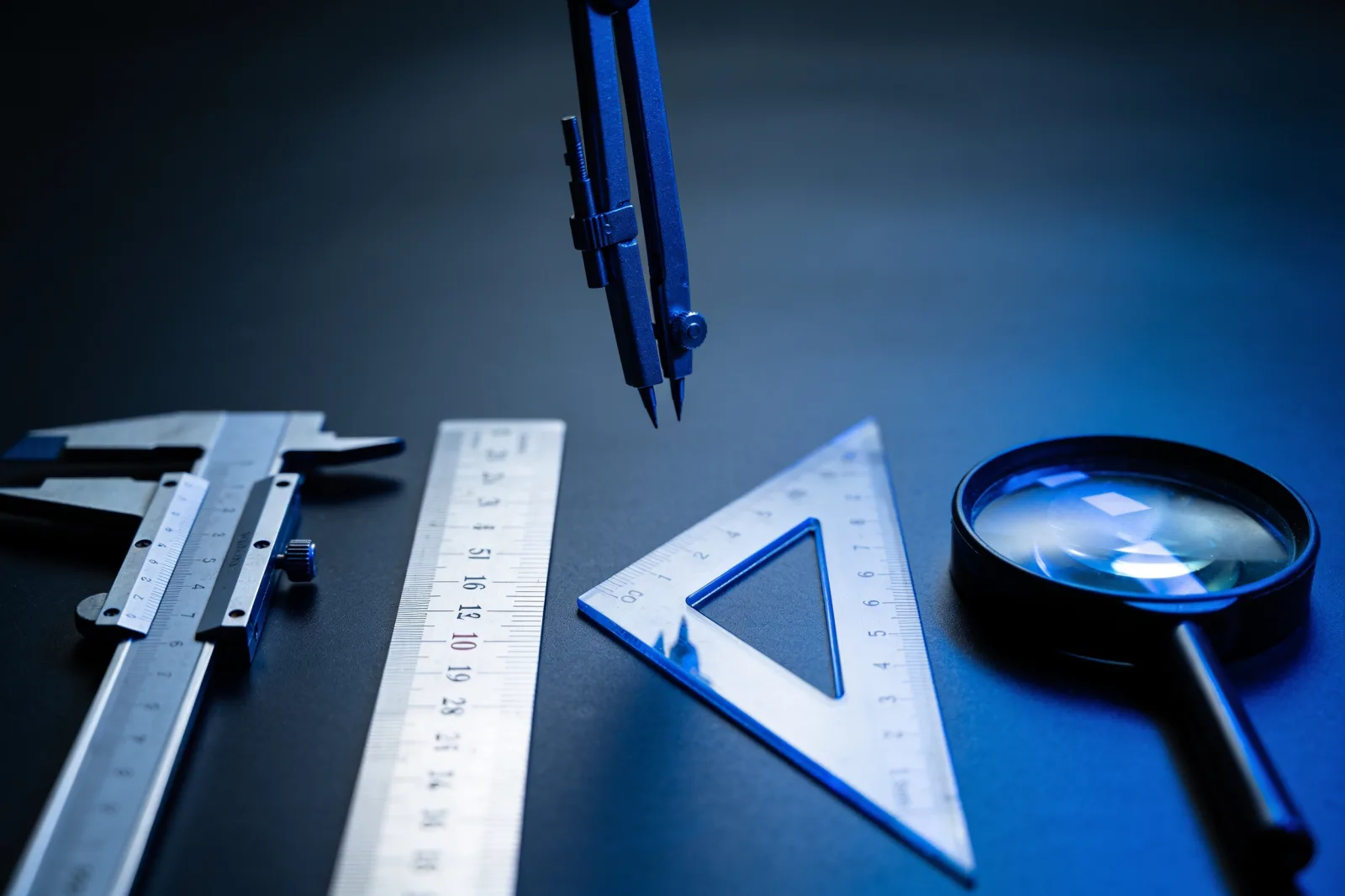 Four precision measuring tools laid out on a dark workbench, one lifted as if being chosen